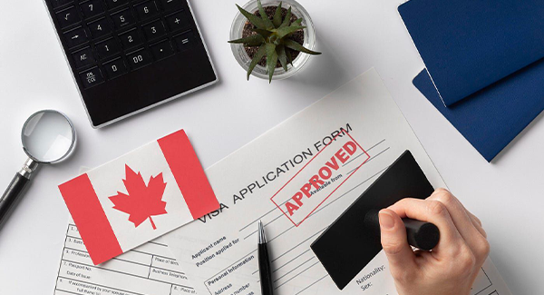 A close-up view of a Canadian visa application form stamped “Approved,” alongside a small Canadian flag, pen, and documents—symbolizing successful immigration and permanent residence approval with the help of Venko Law Firm in Ottawa.