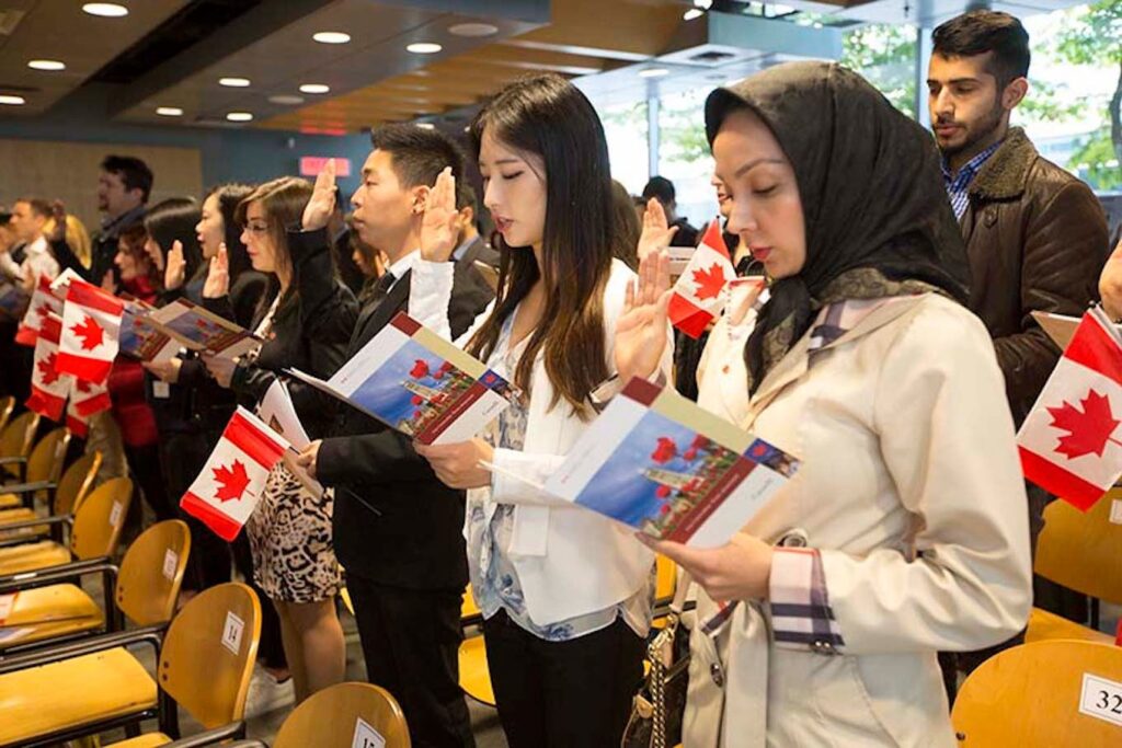New immigrants taking the Canadian citizenship oath while holding flags — Venko Law Firm Ottawa assisting with citizenship, immigration, and refugee applications.