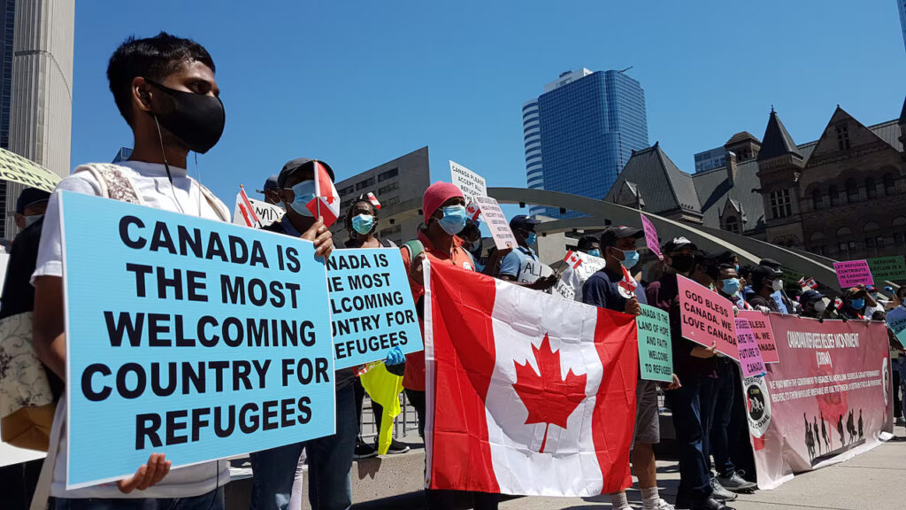Group of refugees and supporters holding Canadian flags and signs that read “Canada is the most welcoming country for refugees” — promoting refugee rights and immigration support in Canada with Venko Law Firm Ottawa.