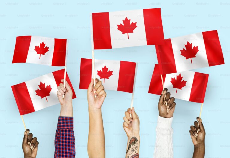 Hands of diverse people proudly waving small Canadian flags, symbolizing immigration and unity in Canada.